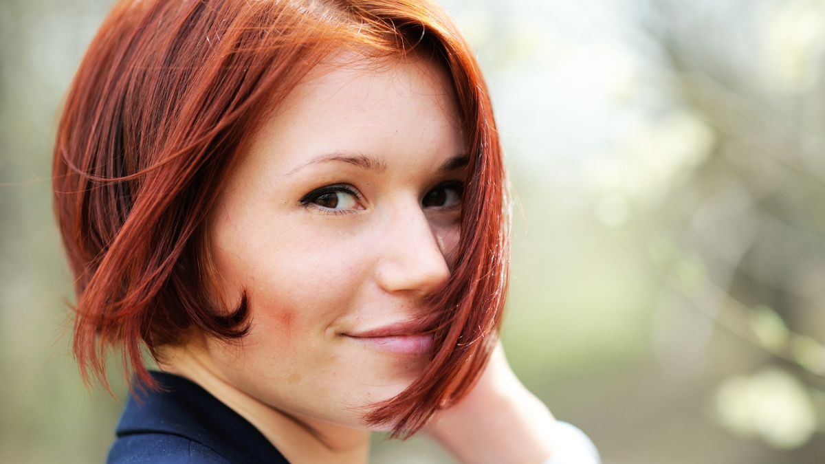 Close-up portrait of beautiful woman with red hair posing outdoors.