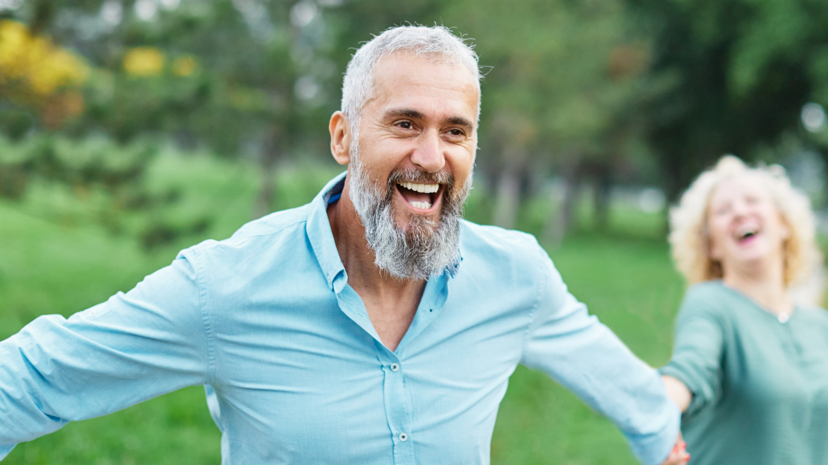 Happy active mid aged adult couple having fun walking running holding hands and bonding in park or nature outdoors.