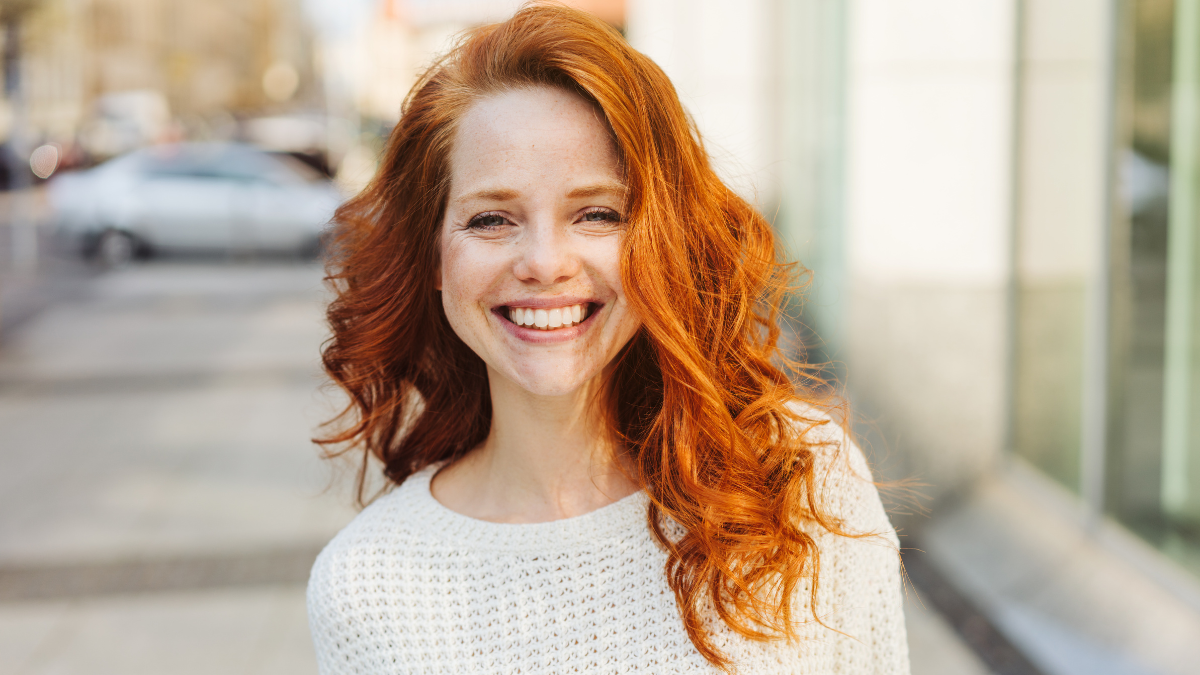 Happy friendly attractive young woman with lovely long curly red hair standing in an urban street grinning at the camera.
