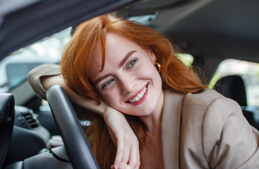 Young Woman Embracing Her New Car. Excited young woman and her new car indoors. Young and cheerful woman enjoying new car hugging steering wheel sitting inside.