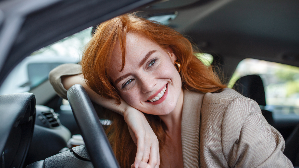 Young Woman Embracing Her New Car. Excited young woman and her new car indoors. Young and cheerful woman enjoying new car hugging steering wheel sitting inside.