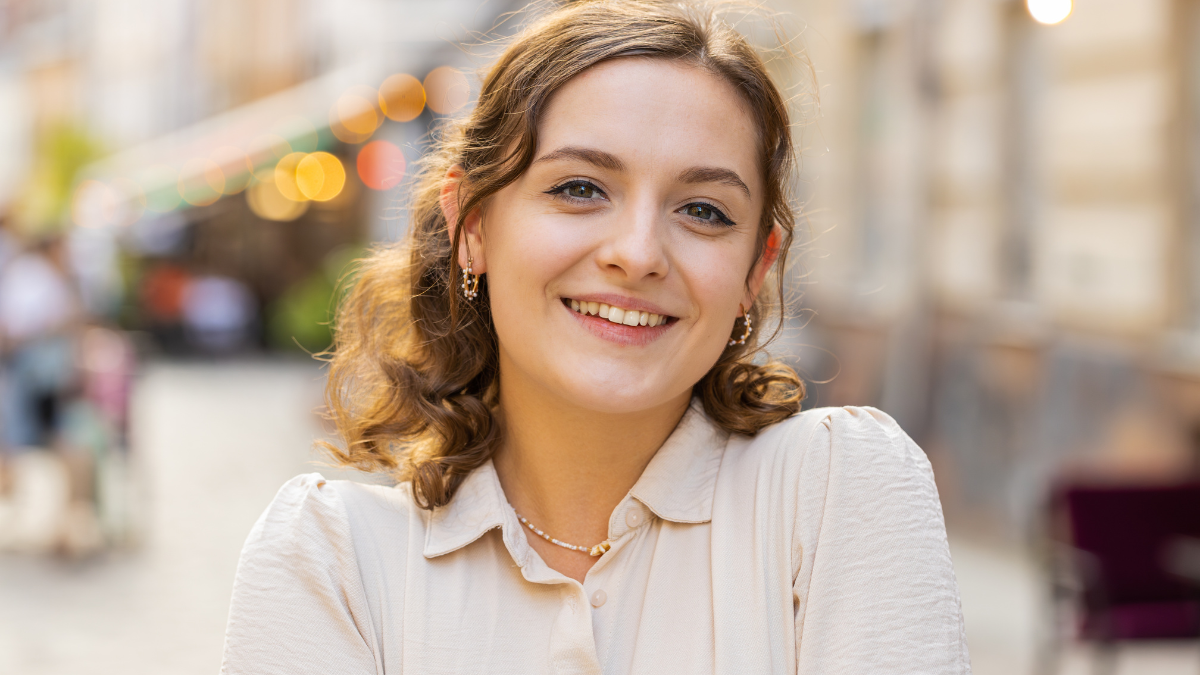 Portrait of happy pretty young woman smiling friendly, glad expression looking at camera dreaming, resting, relaxation feel satisfied good news outdoors. Girl in urban city sunshine street background.