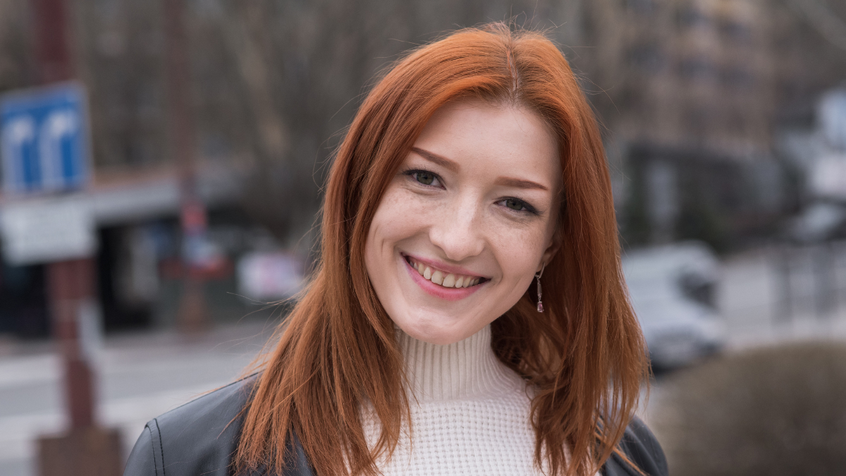 Portrait of a Caucasian redhead young woman wearing white sweater, leather jacket and jeans, posing outdoors on a autumn day. Style, fashion, casual.