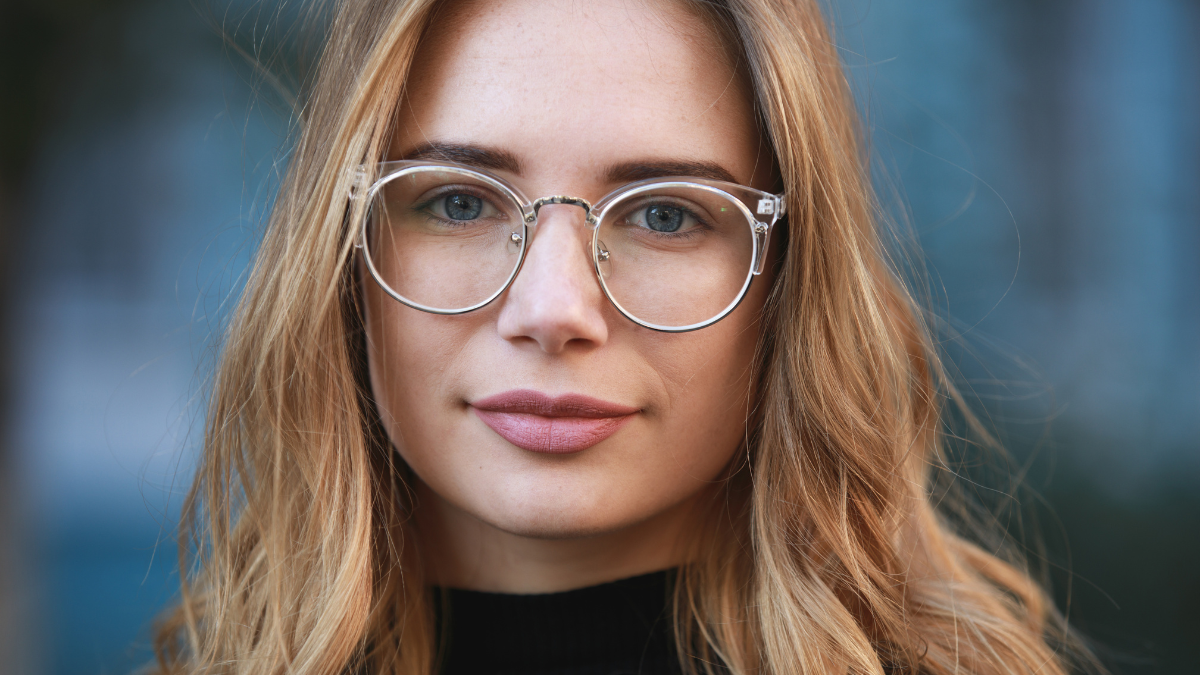 Myopia, close-up portrait of young woman student in eyeglasses for good vision look at camera, blue building background.