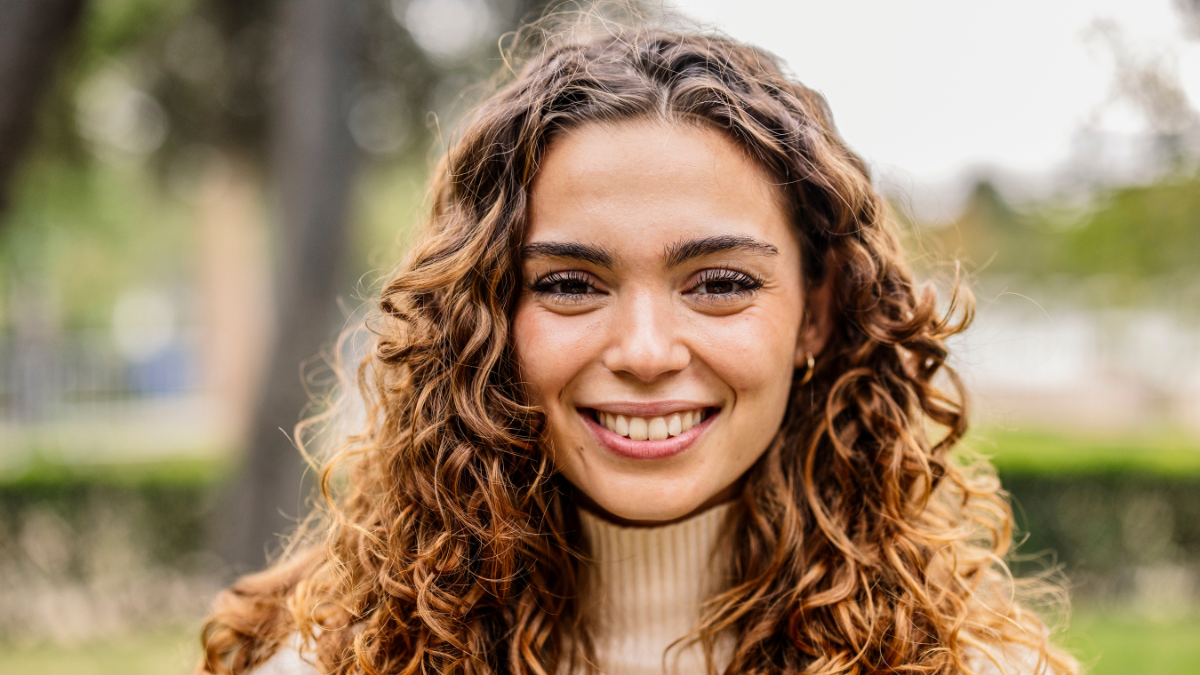 A woman with stunning curly hair beams with a captivating smile in nature.