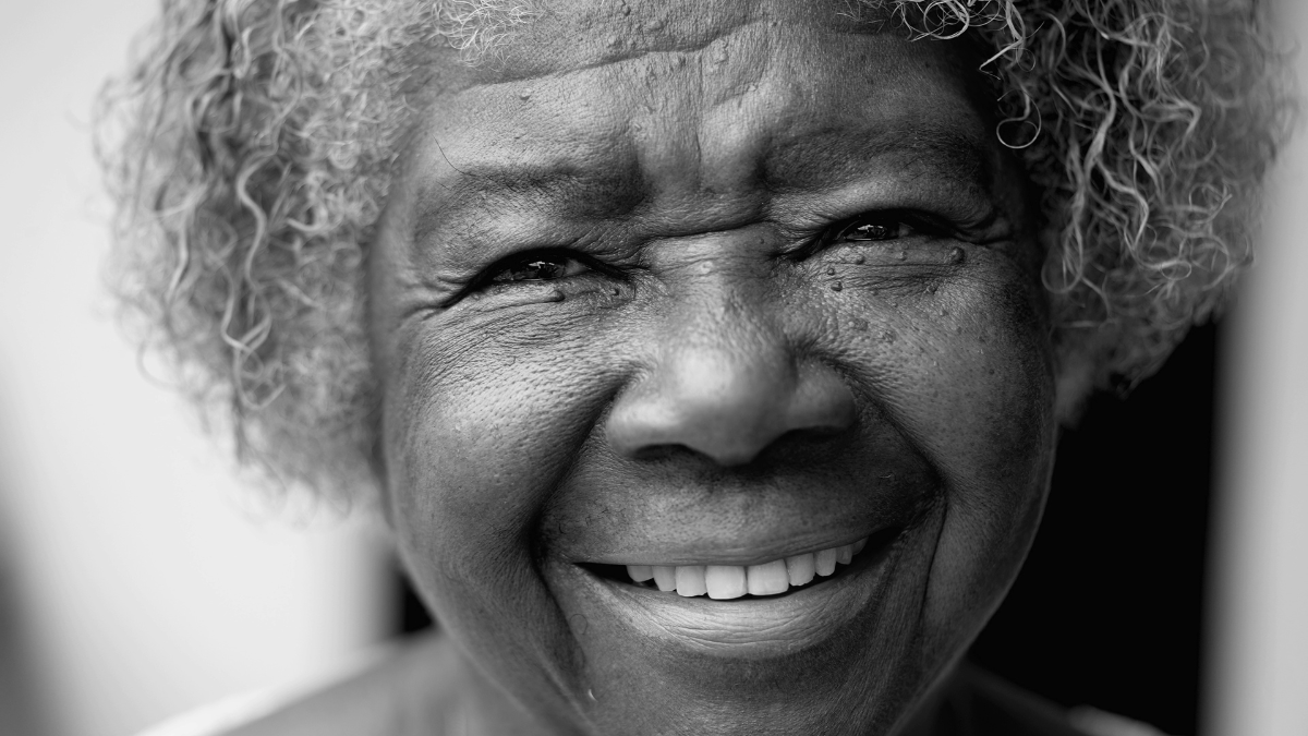 One happy black senior woman in 80s in black and white. Monochromatic portrait of wise older African American lady smiling at camera showing old age and wisdom.