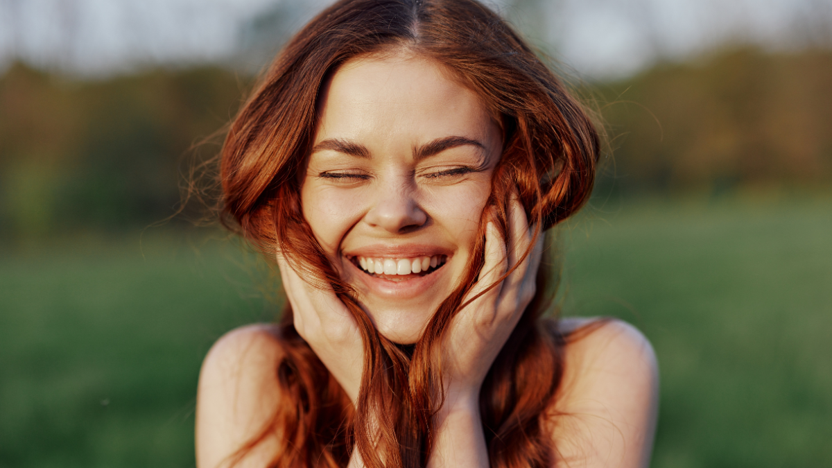 Portrait of a young redheaded woman looking into the camera and smiling, close-up portrait of a laughing woman in the setting sunlight.