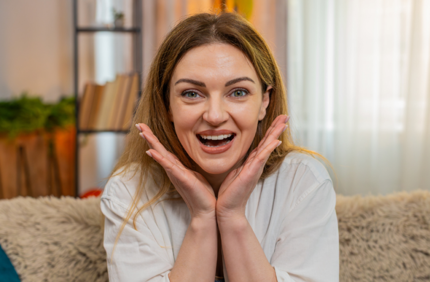 Middle-aged woman looks at camera on home sofa with surprise, saying wow and reacting with big emotion. Young adult girl shows amazement and visible shock, overwhelmed by unexpected moment or news.