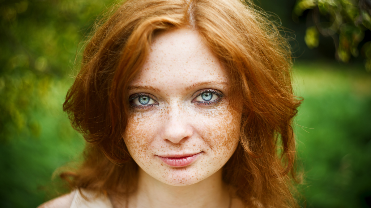 Portrait of redhead girl with blue eyes on nature. Face of young woman with freckles closeup.