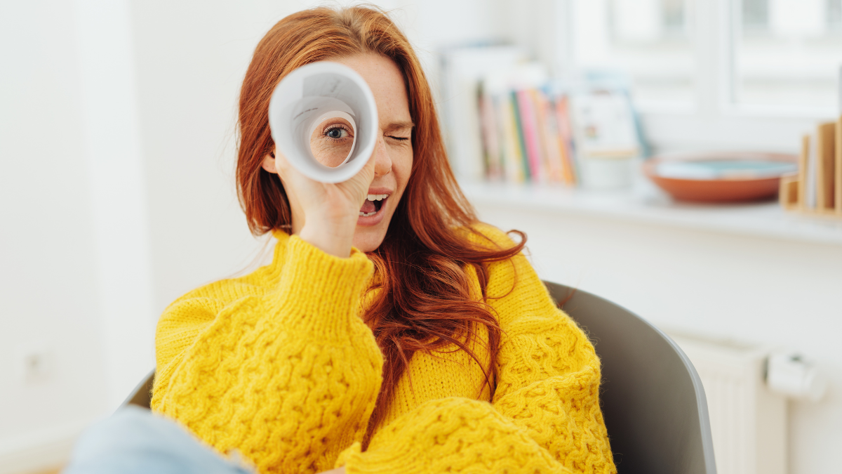 happy redhead woman looking through paper telescope.