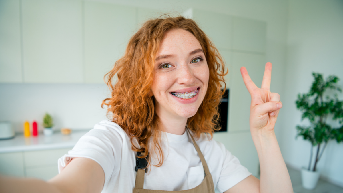 Charming young woman with red hair wearing an apron, smiling indoors in a modern kitchen.