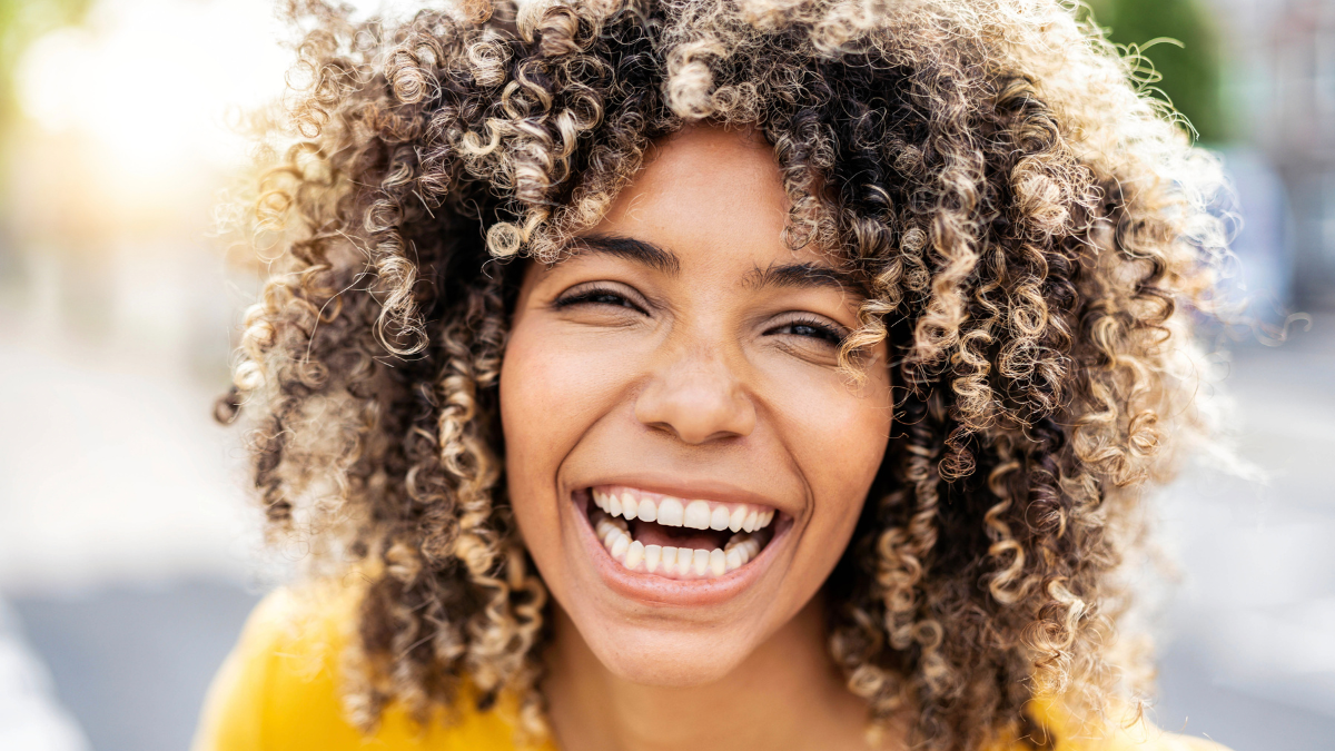Happy afro american young woman smiling at camera outside - Close up portrait of brazilian female laughing on city street - Life style and positive vibes people concept.