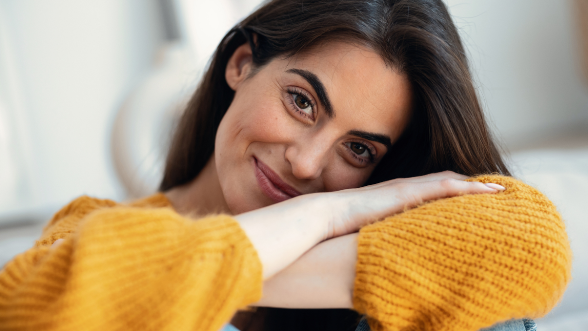 Portrait of scute young woman looking at camera while sitting on sofa at home.