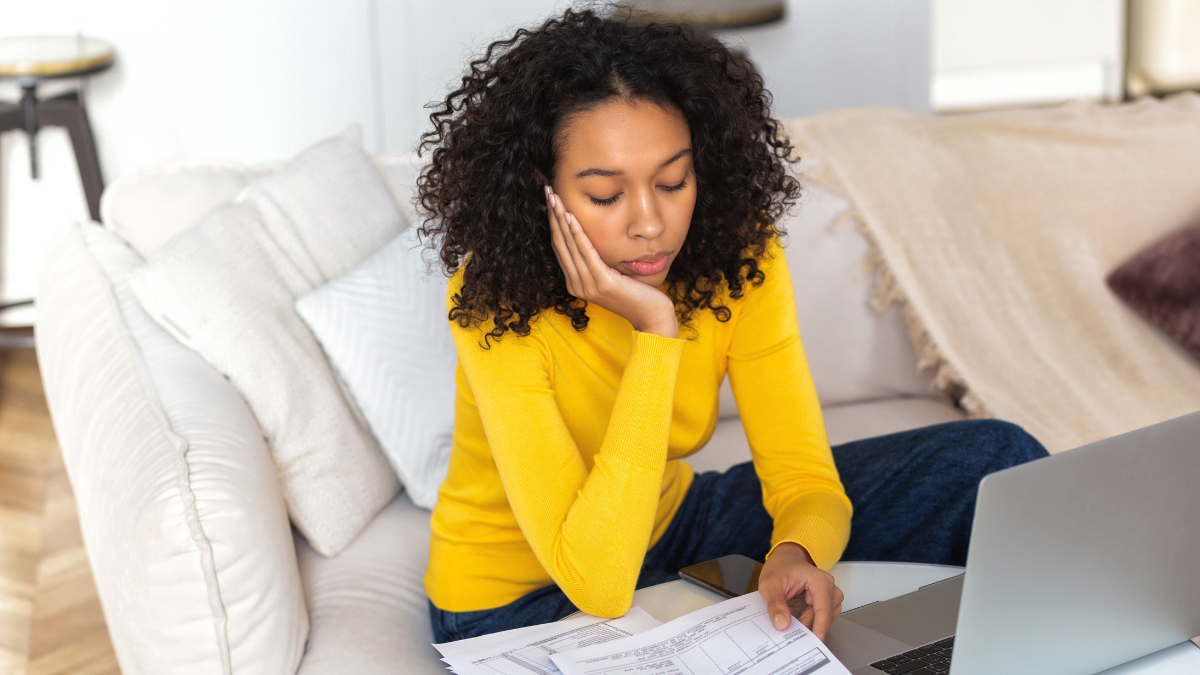 Problems concept. African American woman analyzing budget or utility bills, looking worried sitting at home on the sofa.