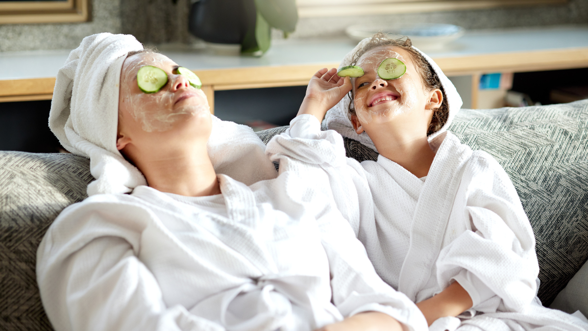 Fresh skincare, face mask and healthy skin treatment for bonding mother and daughter home spa day. Fun, smiling and playful child and parent relaxing with cucumber over their eyes in grooming routine.