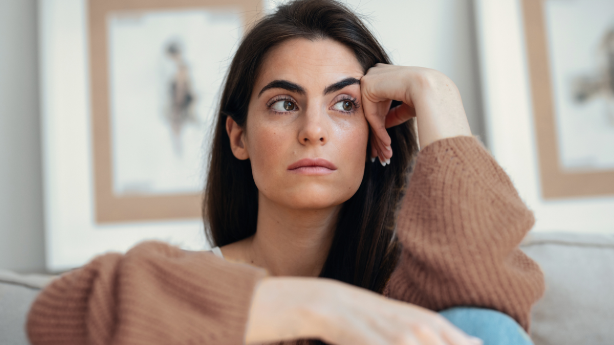 Shot of depressed young woman overthinking while sitting on the couch at home.
