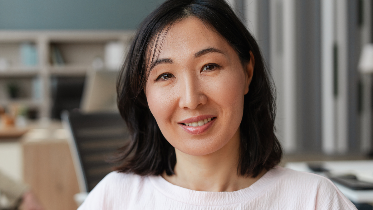 Cheerful asian woman with beautiful black hair smiling in office sitting, exuding confidence and professionalism.