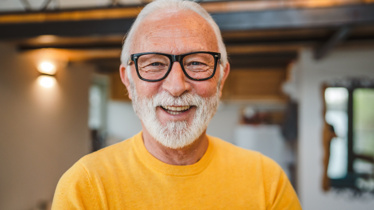 One modern senior caucasian man portrait of male grandfather with beard stand in his house in day wear yellow sweater happy confident copy space portrait.