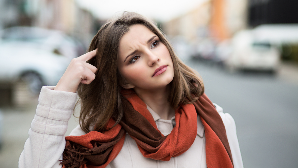 Woman trying to remember Closeup portrait headshot young lady girl scratching head thinking daydreaming deeply about something looking up isolated cityscape outdoor background Multicultural mixt race.