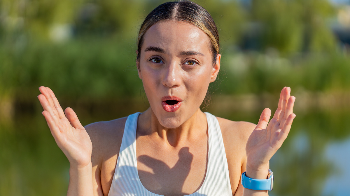 Oh my God, Wow. Athletic fitness runner girl woman touches face in surprise looking at camera with big eyes, shocked by sudden victory. Sportswoman workout cardio training outside in sunny city park.