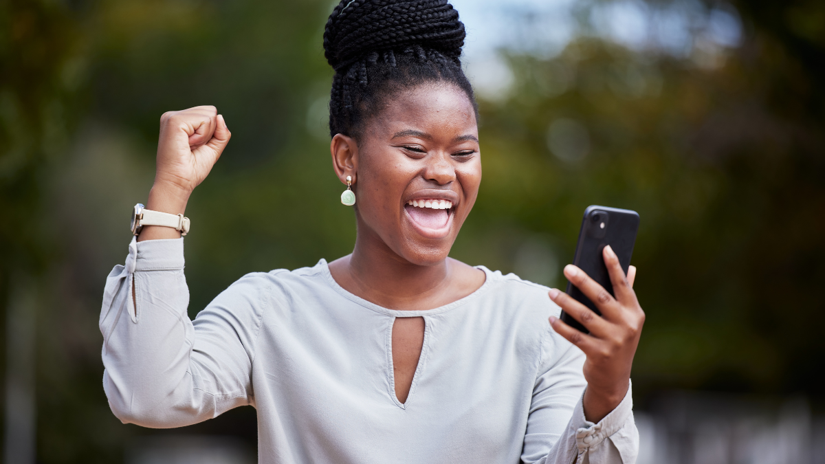 Happy black woman, phone and winner for good news, promotion or business opportunity in the outdoors. African American woman with smile in excitement for bonus, achievement or victory on smartphone.