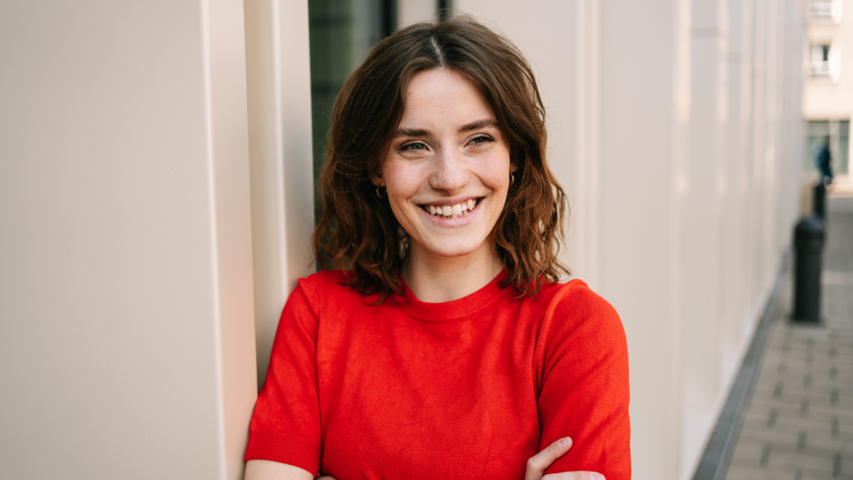 Young Woman in Red Sweater Leaning and Laughing by Modern Building.
