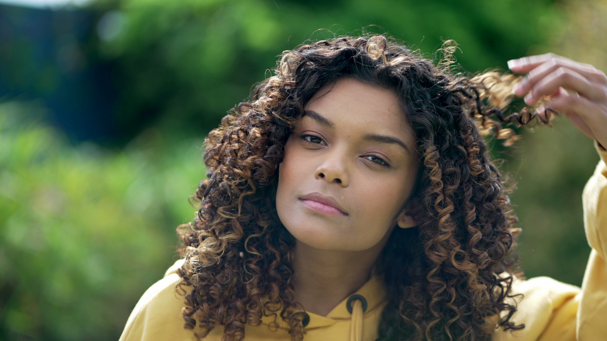 A black hispanic latina girl adjusting curly hair looking at camera. Portrait face closeup of young woman.