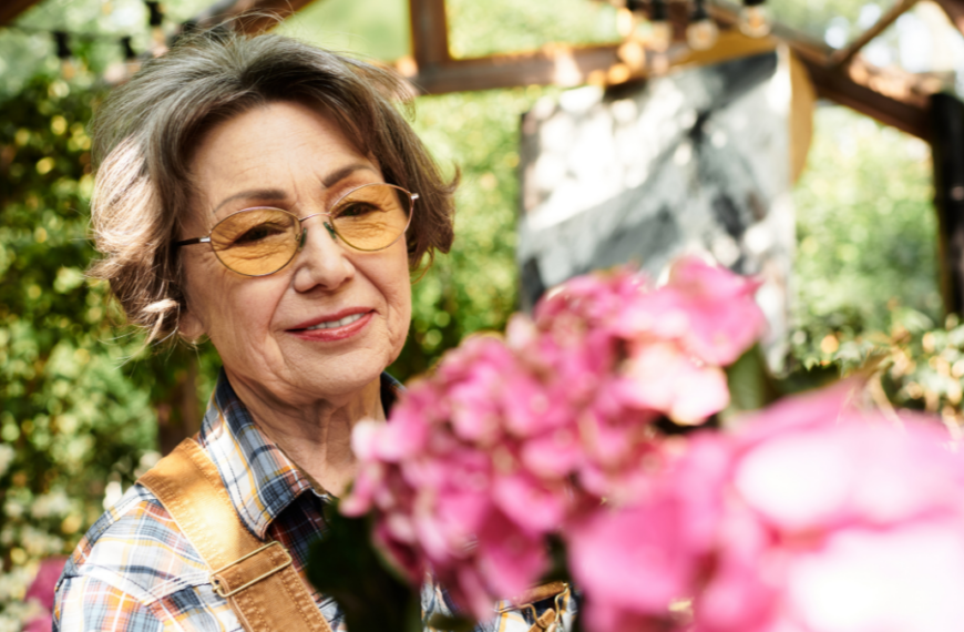 A lovely senior woman nurtures vibrant flowers in her serene, sunlit garden oasis.