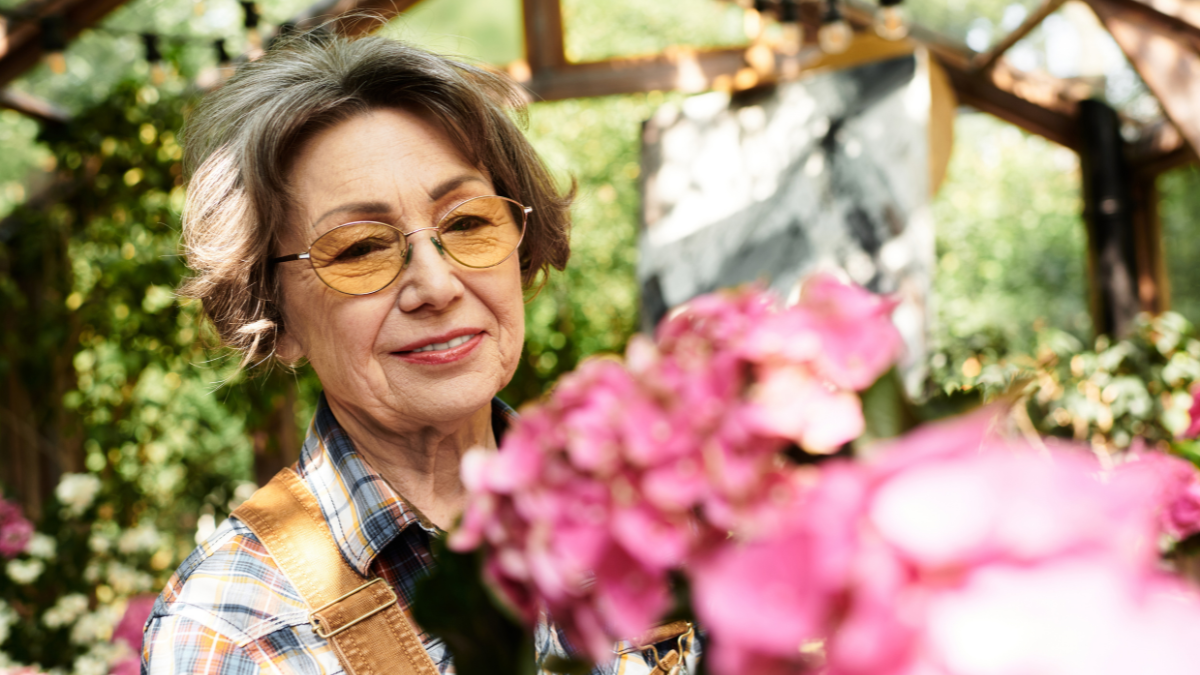 A lovely senior woman nurtures vibrant flowers in her serene, sunlit garden oasis.