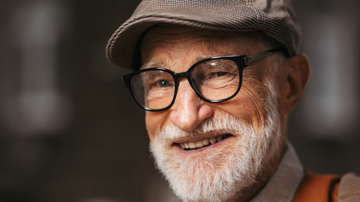 Studio portrait of a senior man with glasses and a beret on his head.