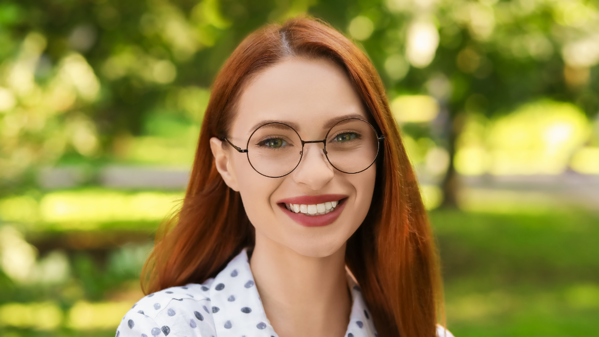 Portrait of happy young woman with glasses outdoors. Lady with beautiful smile looking into camera.