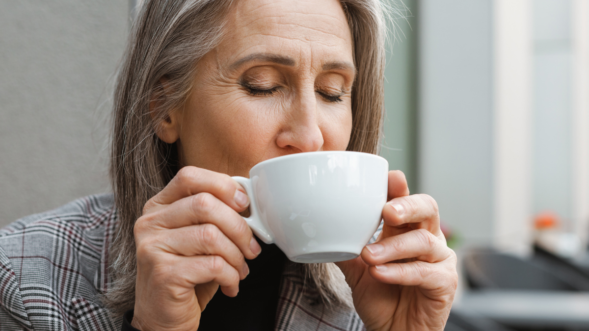 Grey white senior woman drinking coffee while sitting in cafe outdoors.