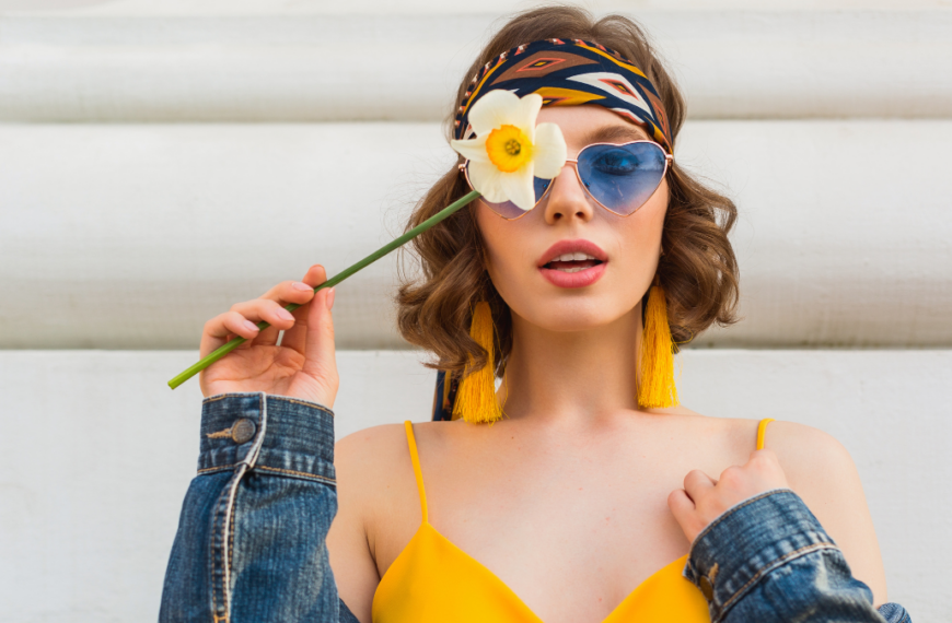 beautiful sexy woman in yellow stylish dress wearing denim jacket, holding flower, trendy outfit, hippie indie style, spring summer fashion trend, blue sunglasses, street fashion, trendy accessories.