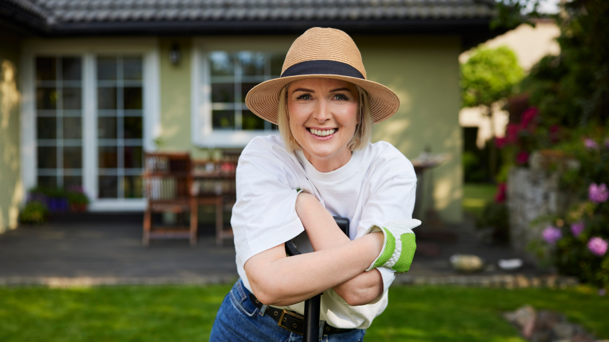 Portrait of happy adult woman leaning on shovel standing in backyard garden.