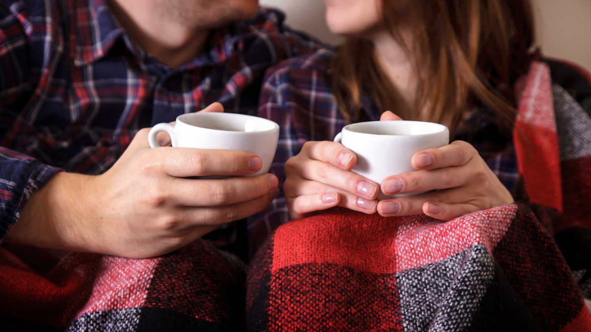 Young couple's hands with two cups of hot coffee. Man and woman together in a warm blanket.