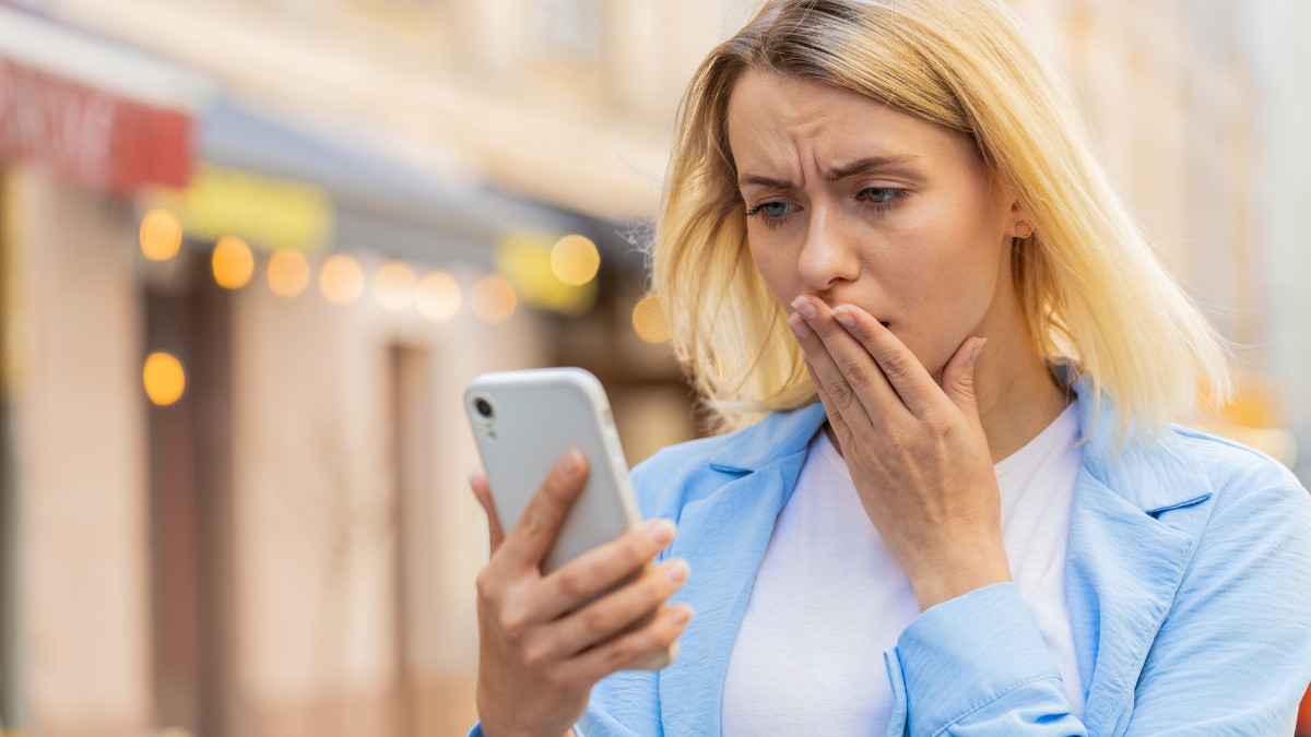 Sad Caucasian young woman using smartphone browsing loses becoming surprised sudden lottery results bad news fortune loss app fail virus thief fraud outdoor. Tourist lady standing on urban city street.