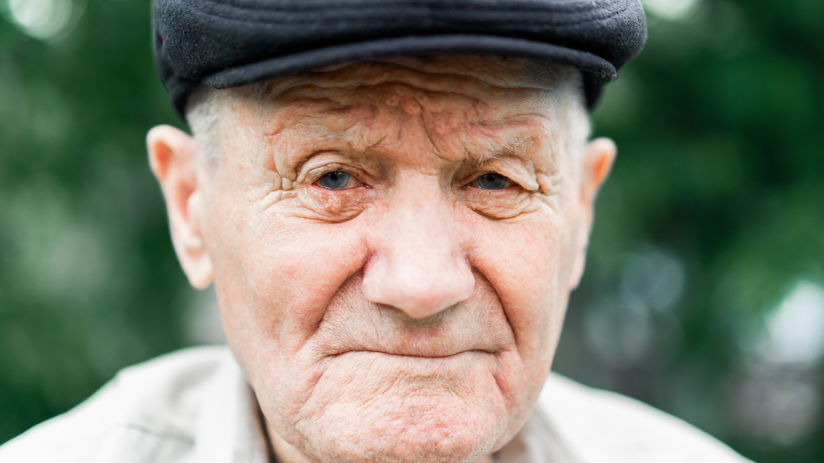 Very old caucasian man portrait. Grandfather in hat. Portrait: aged, elderly, loneliness, senior with lot of wrinkles on face. Close-up of a pensive old man sitting alone outdoors.