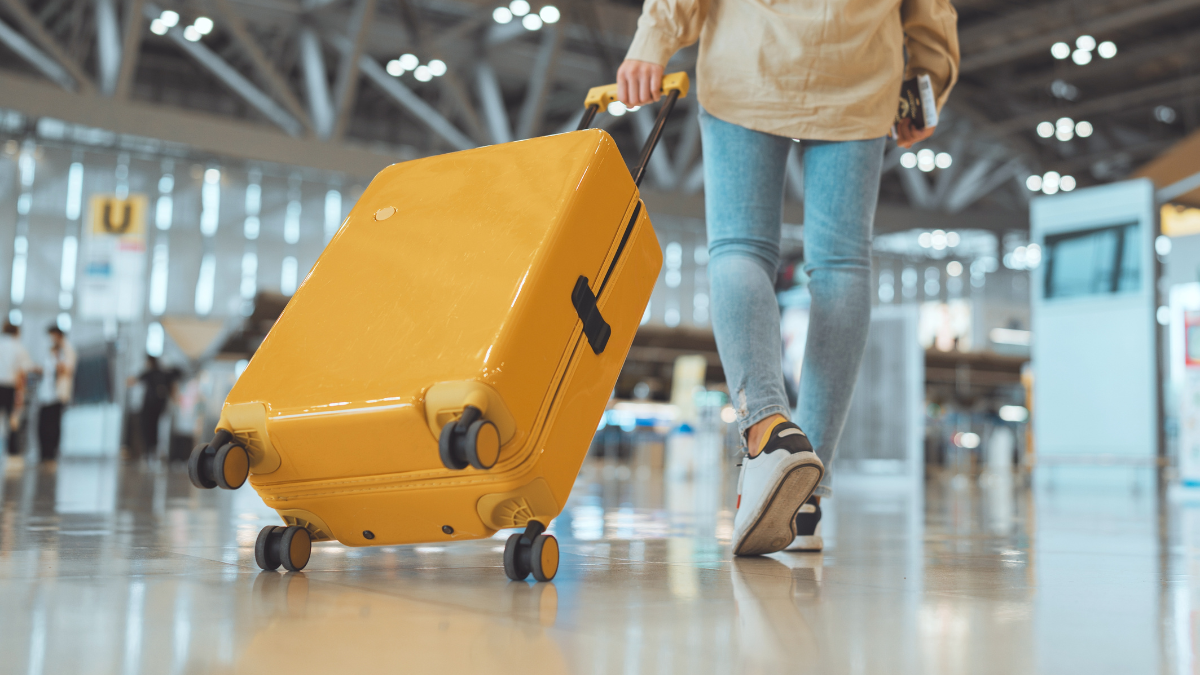 Female traveler passenger walking with a yellow suitcase at the modern Airport Terminal, Back view of woman on her way to flight boarding gate, Ready for travel or vacation journey.