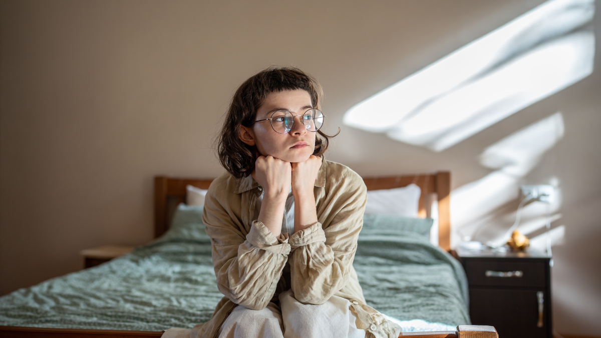 Depressed lonely woman sitting on cozy bed sadly look at window feeling anxiety. Alone girl suffering from emotional pain having life troubles, problems. Mental disorder anhedonia, stress discomfort.