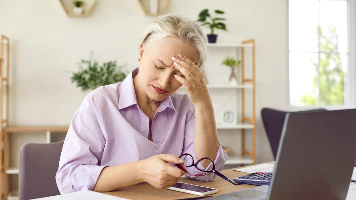 Mature woman feeling tired and suffering from a headache after working on her laptop computer for a long time. Tiredness, overworking, stress, pain, health problems concept.