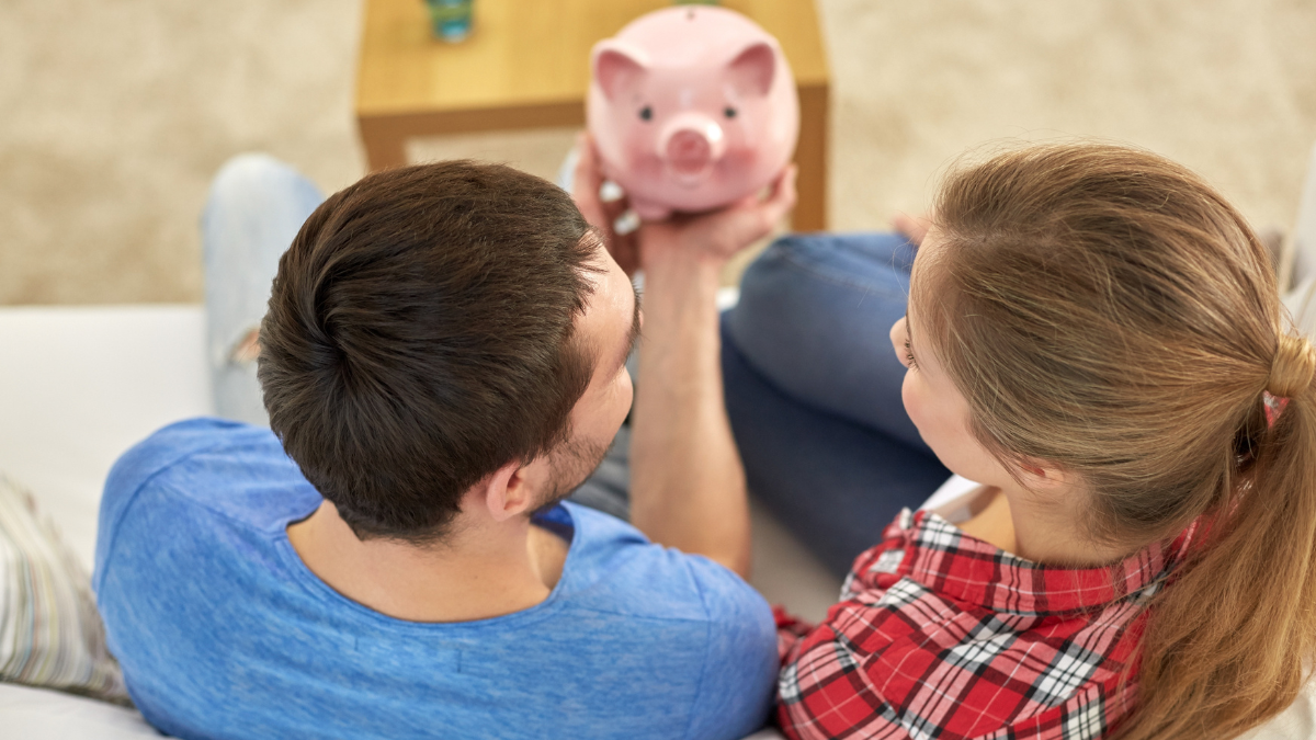 money, home, finance and relationships concept - close up of couple with piggy bank sitting on sofa.