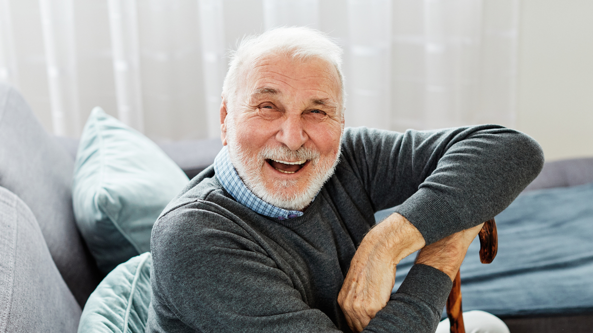 Portrait of a disabled senior man with a walking cane stick at home.