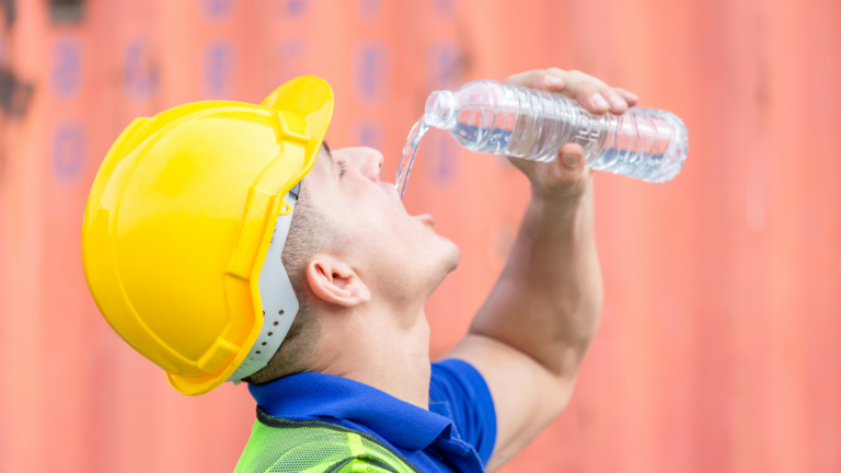 Worker man in hard hat drinking water at containers cargo.