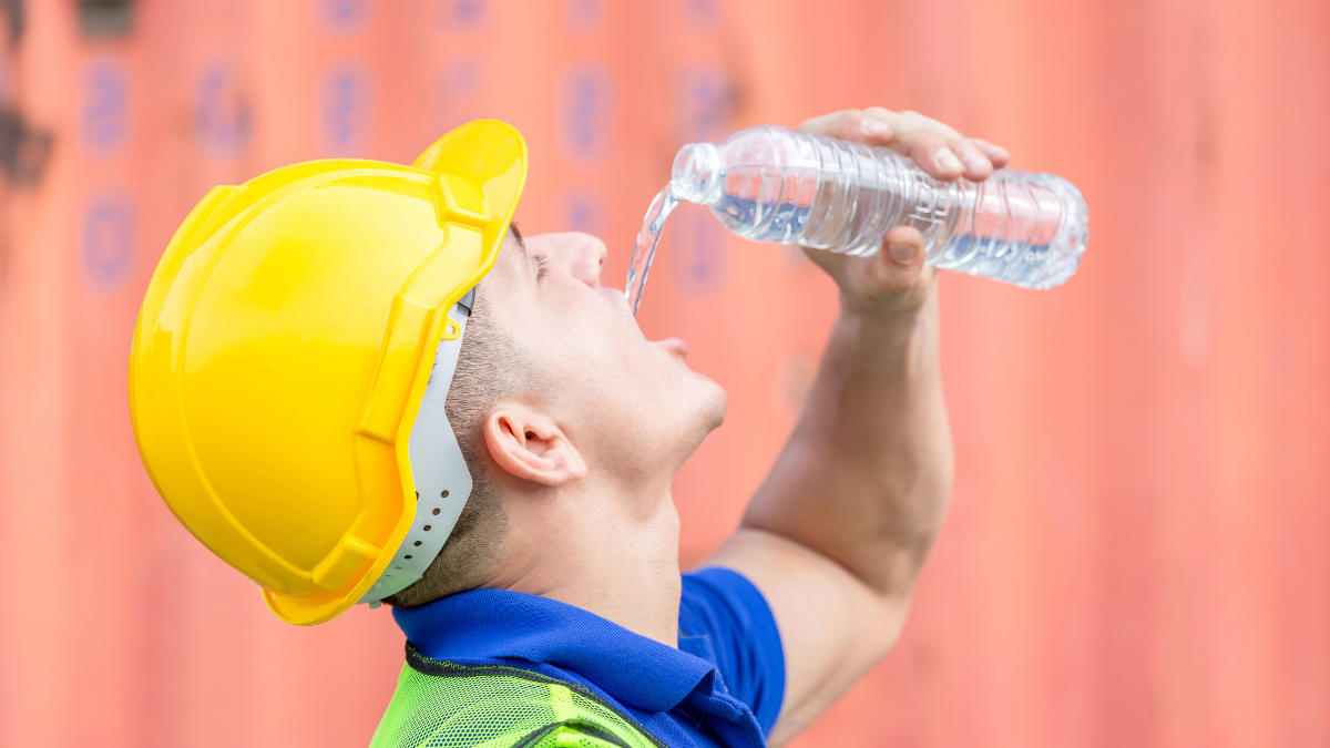 Worker man in hard hat drinking water at containers cargo.