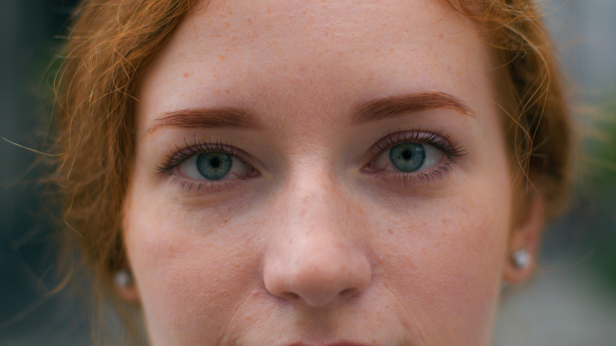 Close up beautiful smiling young Caucasian ginger woman face female lady girl slowly wide opening bright blue eyes looking camera outside city urban street. Clear vision makeup eyesight ophthalmology.