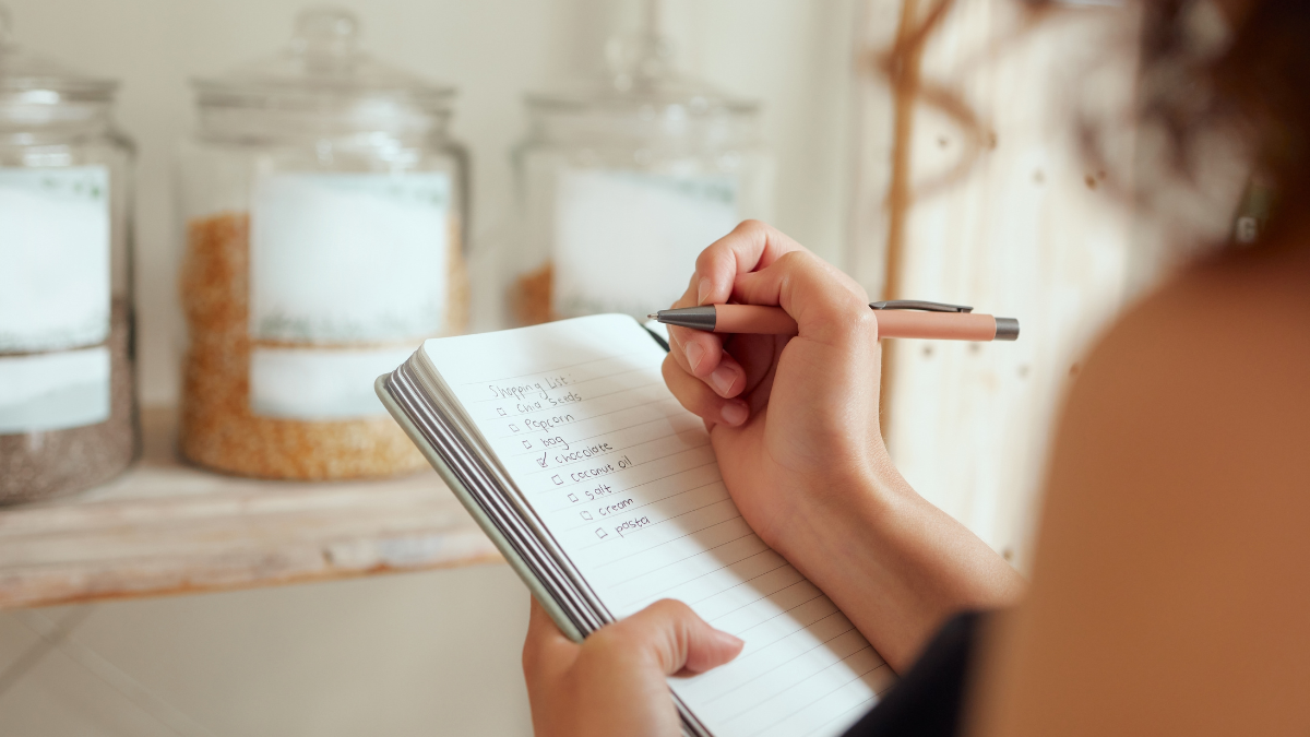 Budget planning, making shopping list and managing household expenses to save money. Financial accountability at home. Woman making shopping list for groceries on a notebook to plan a meal for.
