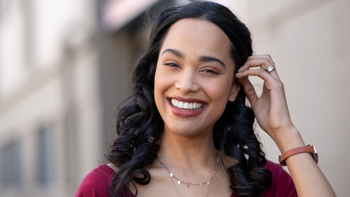 Happy young latin beautiful woman walking on city street. Portrait of carefree hispanic girl smiling and looking at camera. Joyful brazilian woman with long black hair smiling with copy space outdoor.