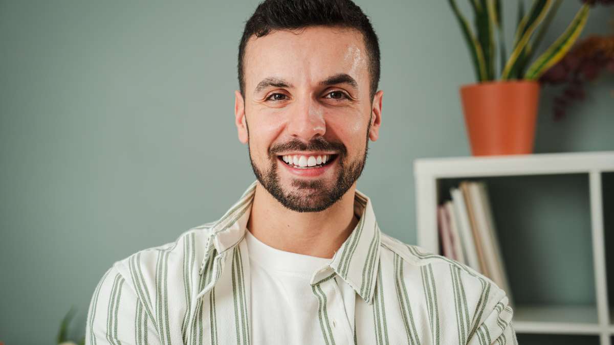 Close up portrait of one handsome guy with perfect white teeth smiling at home. Front view of young confident man with friendly and positive expression. Happy adult male laughing and looking at camera.
