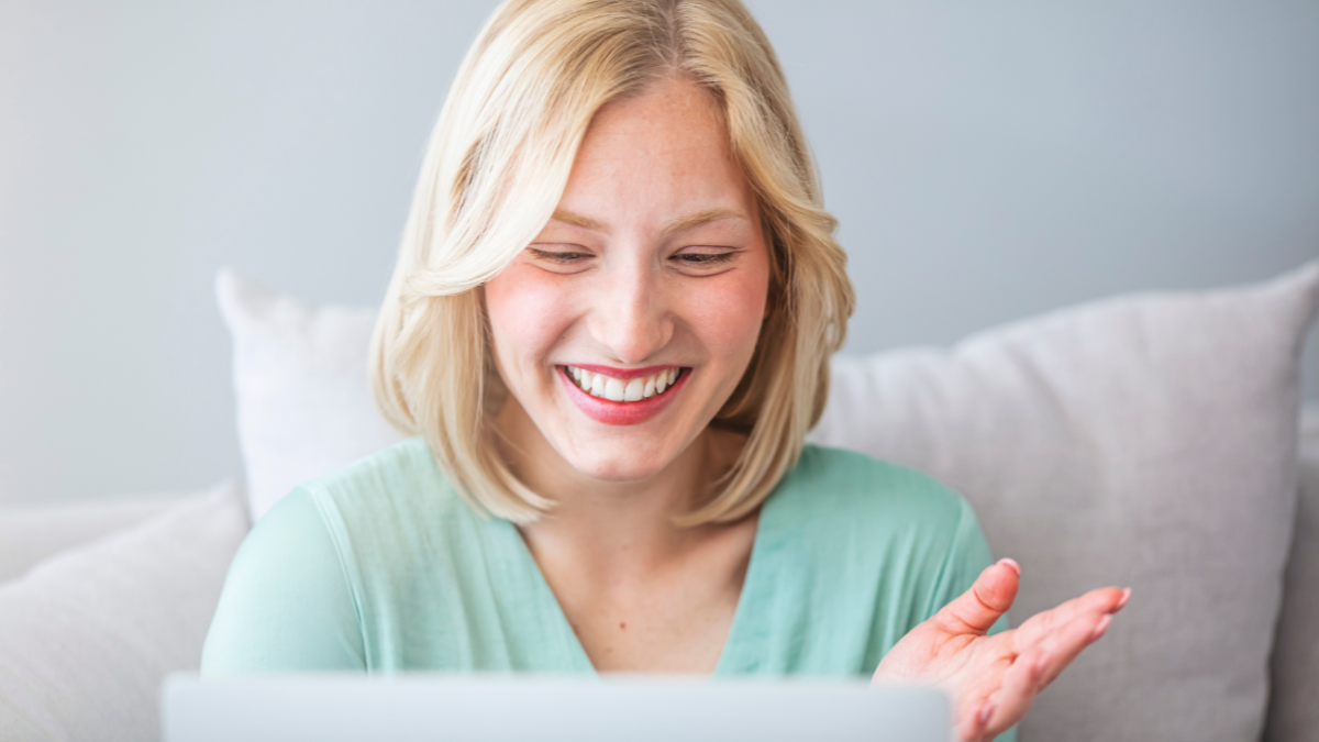 Smiling young Caucasian woman take online educational course or training on laptop from home, happy female wave to camera, talk on webcam video call on computer for her best side hustles.