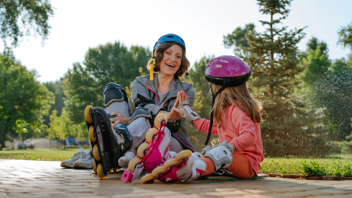 Active happy grandmother and granddaughter giving high five preparing for roller skating sitting in the park. Selective focus on the woman.